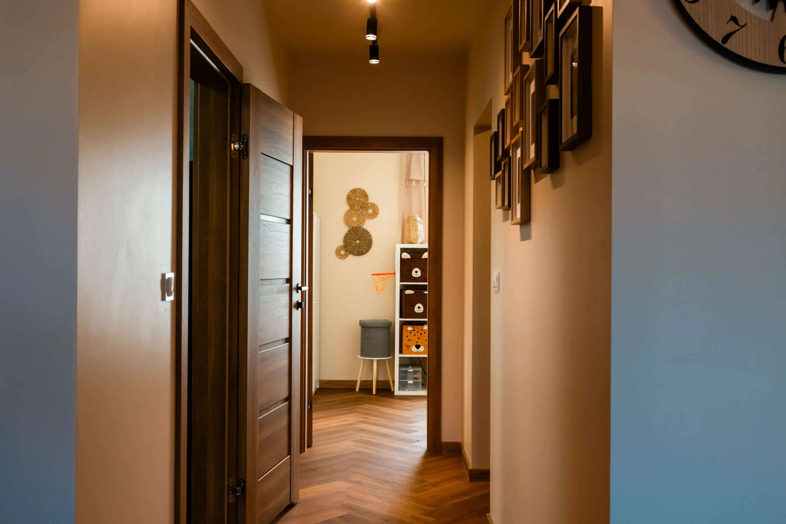 Nowoczesne wykończenie wnętrz w Szczecinie: korytarz z drewnianą podłogą w jodełkę, eleganckimi drzwiami i galerią zdjęć na ścianie w jasnym odcieniu.